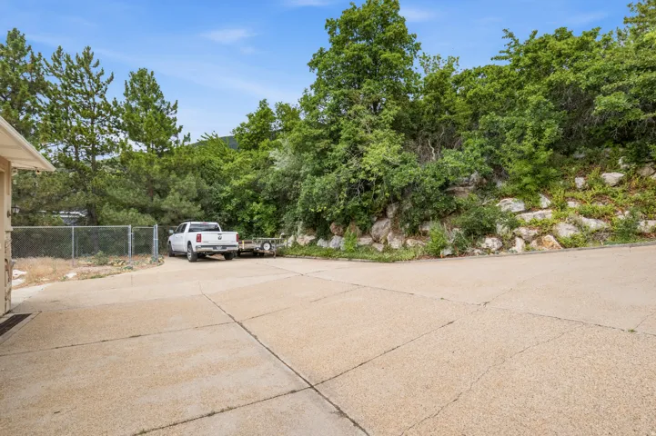 Expansive concrete driveway with a gravel aggregate finish, bordered by mature trees and natural rock landscaping