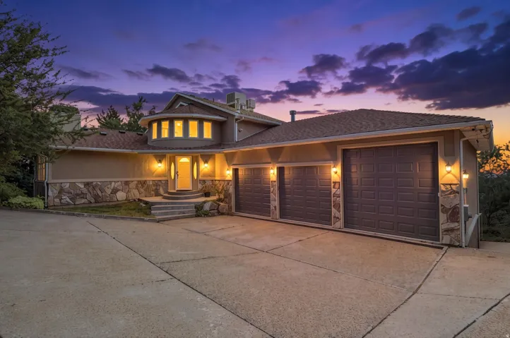 Exterior facade featuring a three-car garage, stone veneer accents, an elevated entry with steps, and a circular architectural element with multiple windows