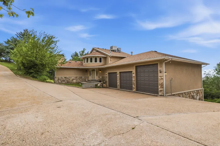 Stucco exterior with stone accents, a multi-car garage, and a curved driveway