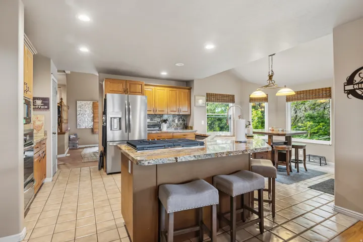 Kitchen featuring a central island with a built-in cooktop, light-toned wood cabinetry, stainless steel appliances, tile flooring, and multiple windows