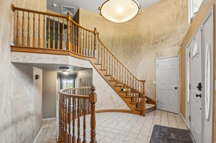 Grand foyer featuring a curved staircase with wood balusters, tile flooring, and a decorative overhead light fixture
