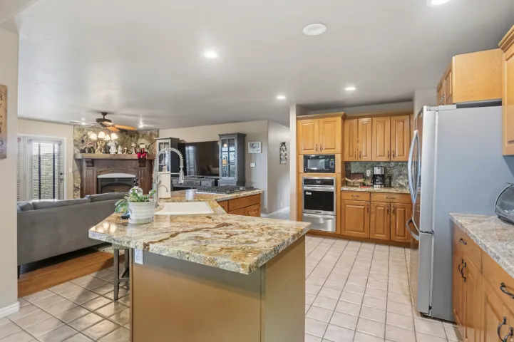 Kitchen featuring a large island with a surface, wood cabinetry, tile flooring, and stainless steel appliances including a built-in microwave and oven