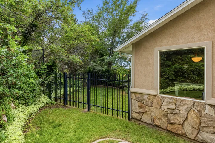 Side exterior featuring a stucco finish, stone veneer detailing, a large picture window, and a black wrought-iron fence