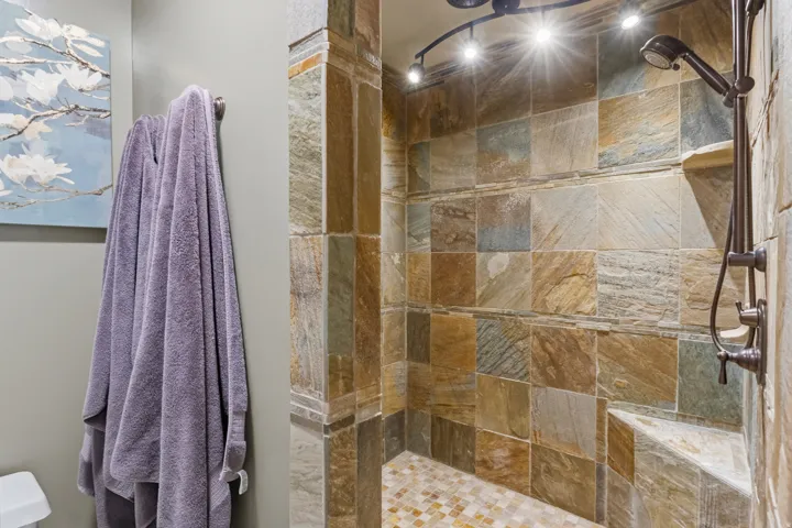 Tiled shower stall featuring a built-in bench, track lighting, and a handheld shower fixture