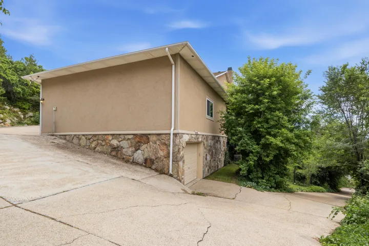 Exterior featuring stucco siding, a stone-clad foundation, and a lower-level garage door