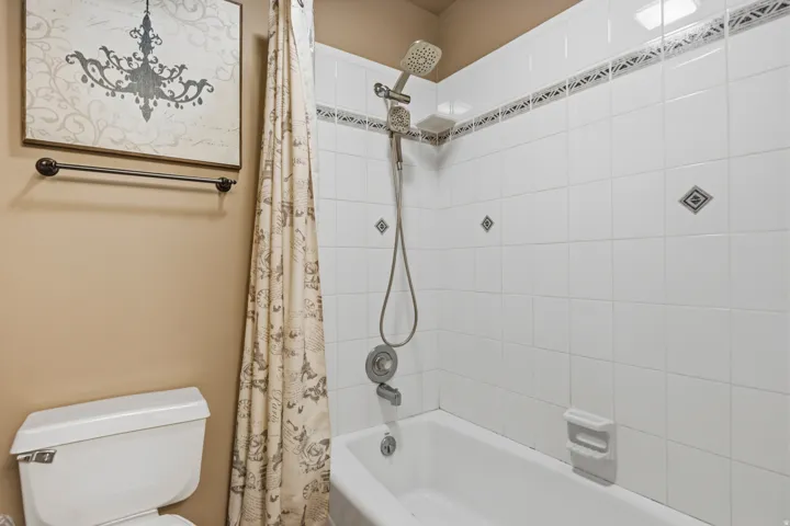 Bathtub with white tile surround, decorative accent tiles, and a multi-function shower head