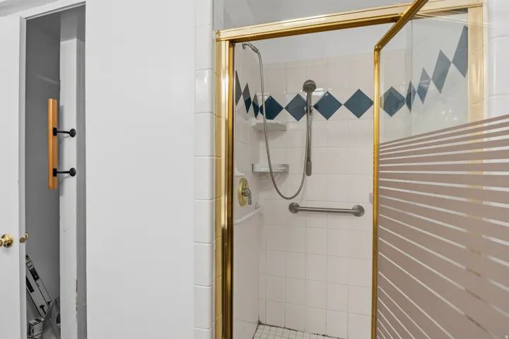 Shower stall with a gold-tone frame, white tiled walls, and decorative blue diamond accents