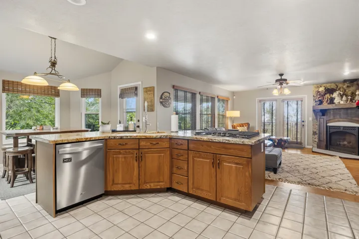 Open-concept kitchen featuring wood cabinetry, granite countertops, an integrated gas cooktop, and a stainless steel dishwasher