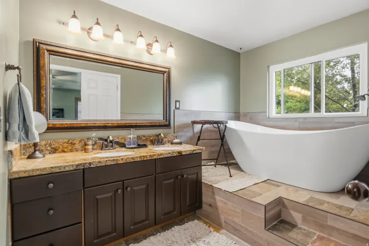 Bathroom featuring a freestanding soaking tub, dual vanity with undermount sinks, bronze hardware, a large framed mirror, and a multi-pane window
