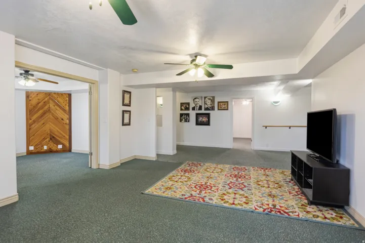 Spacious carpeted room featuring multiple ceiling fans, recessed lighting, and a prominent wood-finish accent wall with a chevron pattern