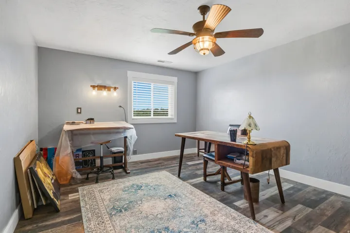Bright interior space featuring wood-finish flooring, a ceiling fan with integrated lighting, and a window with blinds
