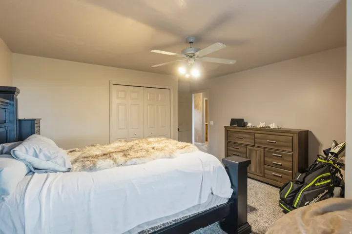 Carpeted bedroom featuring a ceiling fan with integrated lighting, dual bifold closet doors, and neutral wall tones