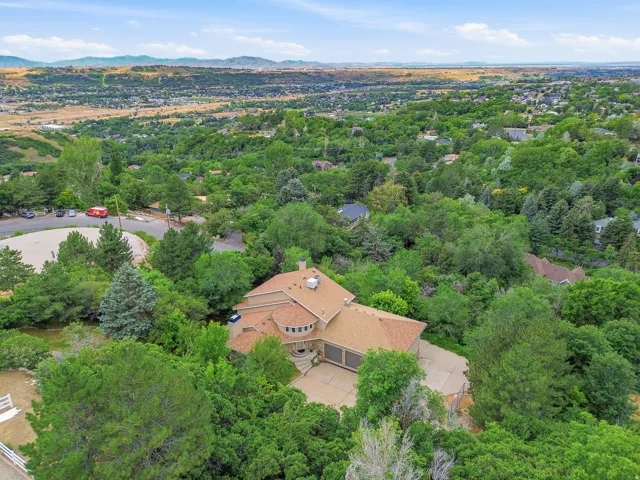 Expansive residential property featuring a large home, mature trees, a multi-car driveway, and a distant mountain backdrop