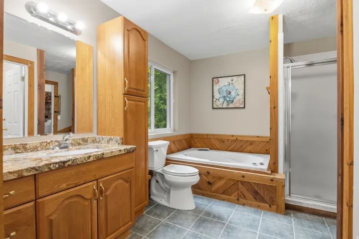 Bathroom featuring a built-in jetted tub, a separate glass-enclosed shower, a vanity with a stone-finish countertop, and wood cabinetry