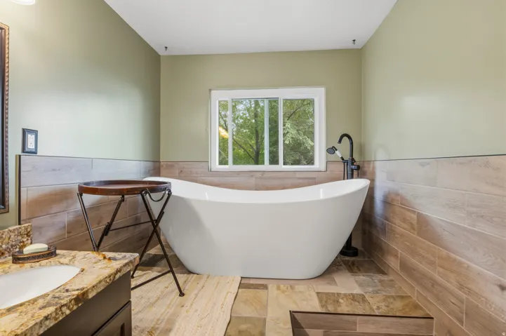 Freestanding soaking tub with a floor-mounted matte black faucet, set against a window