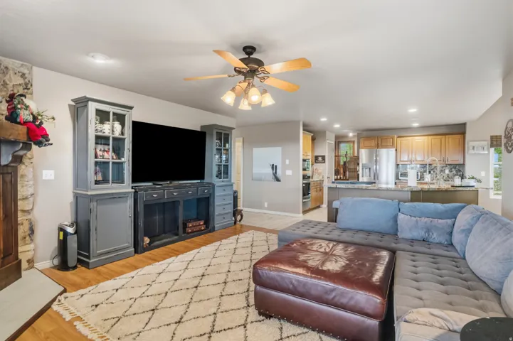 Open-concept living space featuring wood-finish flooring, a stone fireplace, and a ceiling fan with integrated lighting