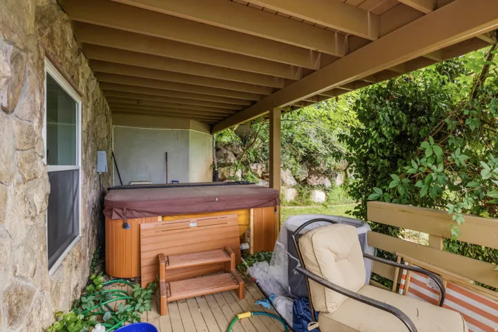 Covered outdoor patio featuring a hot tub, wood-finish decking, and a stone exterior wall