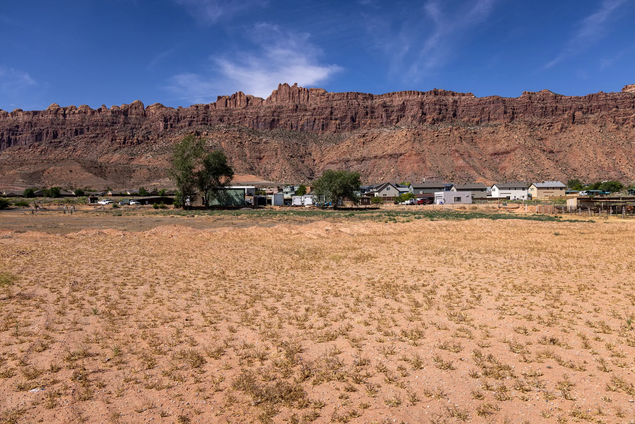 Expansive undeveloped land featuring a desert landscape and distant residential structures, all set against a prominent red rock formation backdrop