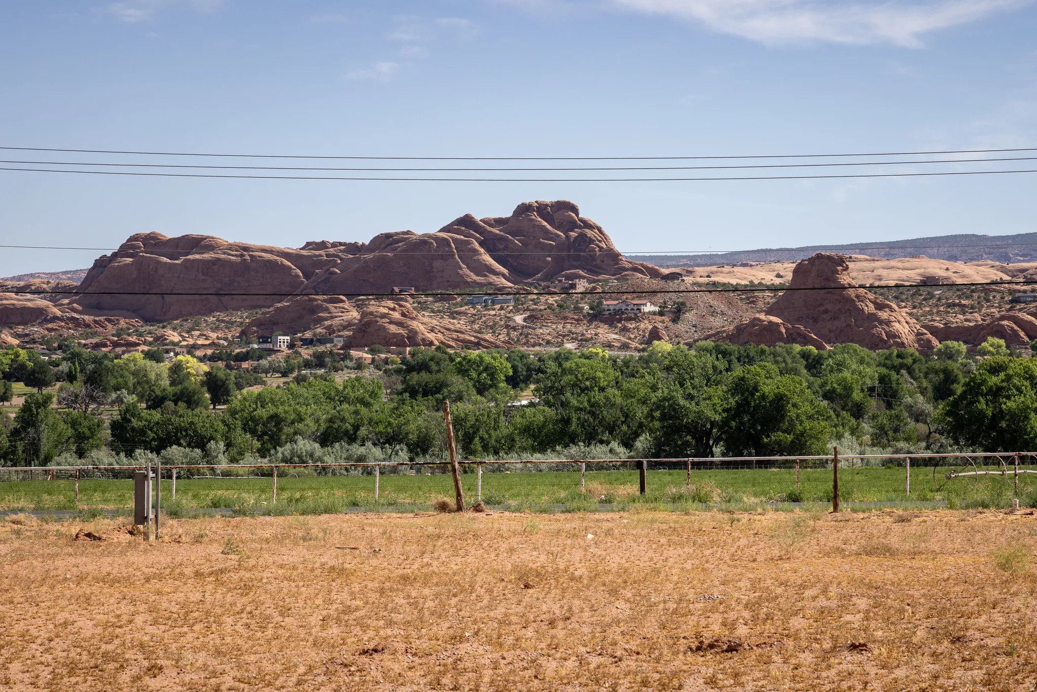 Expansive natural landscape featuring rock formations, green foliage, and a foreground of dry, open land