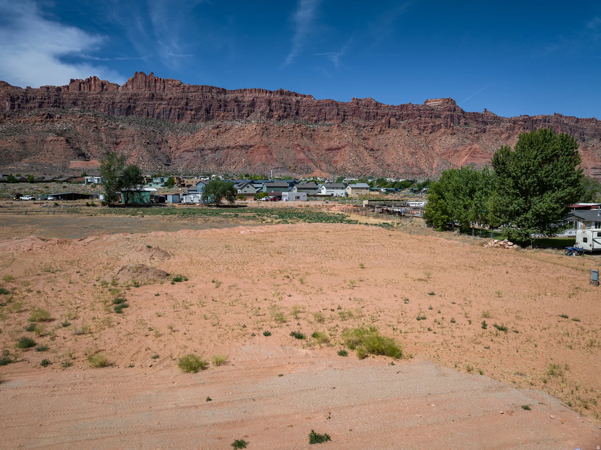 Expansive undeveloped lot featuring a red rock mountain backdrop, distant community structures, and mature trees