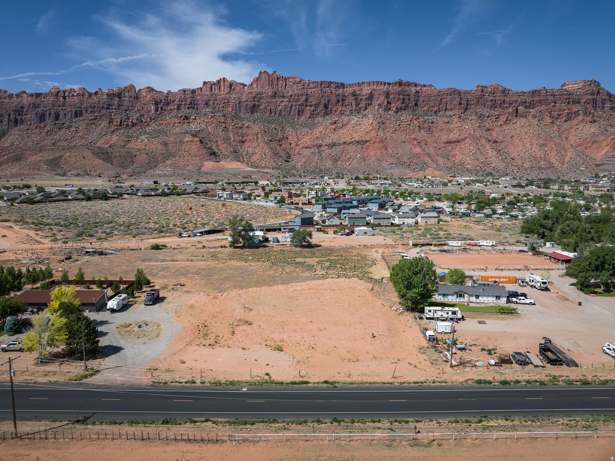 Expansive undeveloped land parcel featuring a dark asphalt road frontage, with distant red rock formations creating a natural backdrop