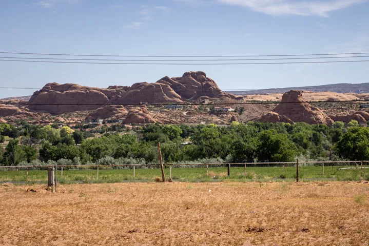 Expansive natural landscape featuring rock formations, green foliage, and a foreground of dry, open land