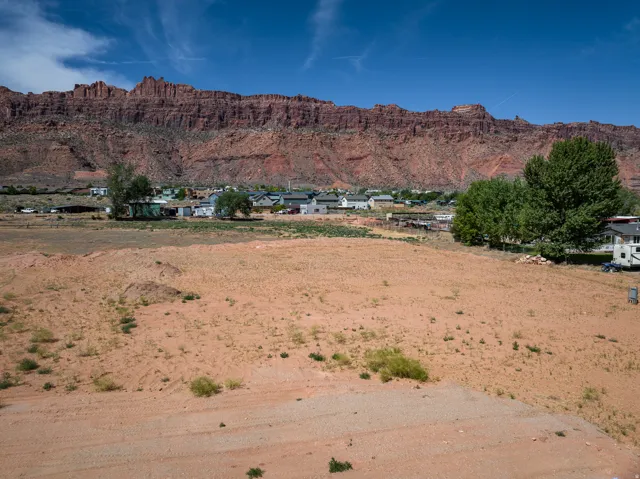 Expansive undeveloped lot featuring a red rock mountain backdrop, distant community structures, and mature trees