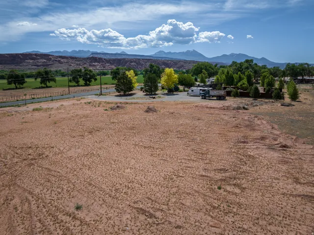 Expansive open land featuring distant mountains, a green valley, mature trees, and a paved road