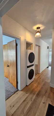 Hallway featuring wood-finish flooring, white walls, and a built-in stacked washer and dryer unit