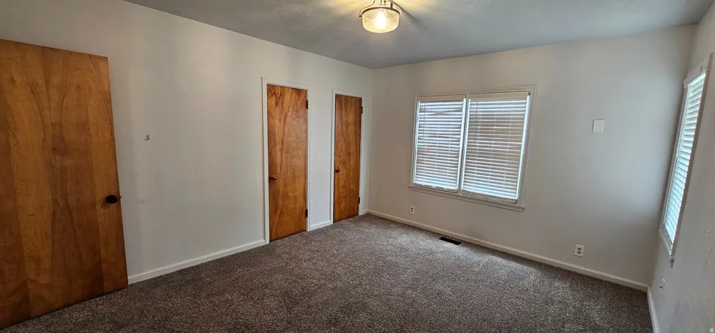 Carpeted interior space featuring white walls, two wood-finish doors, and two windows with blinds