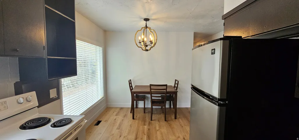 Dining area featuring wood-finish flooring, a contemporary chandelier, and a large window with blinds