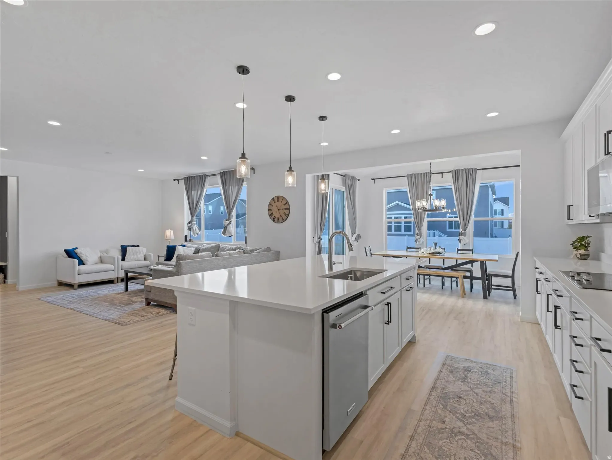 Open-concept living space featuring a central kitchen island with integrated sink, wood-finish flooring, recessed lighting, and large windows