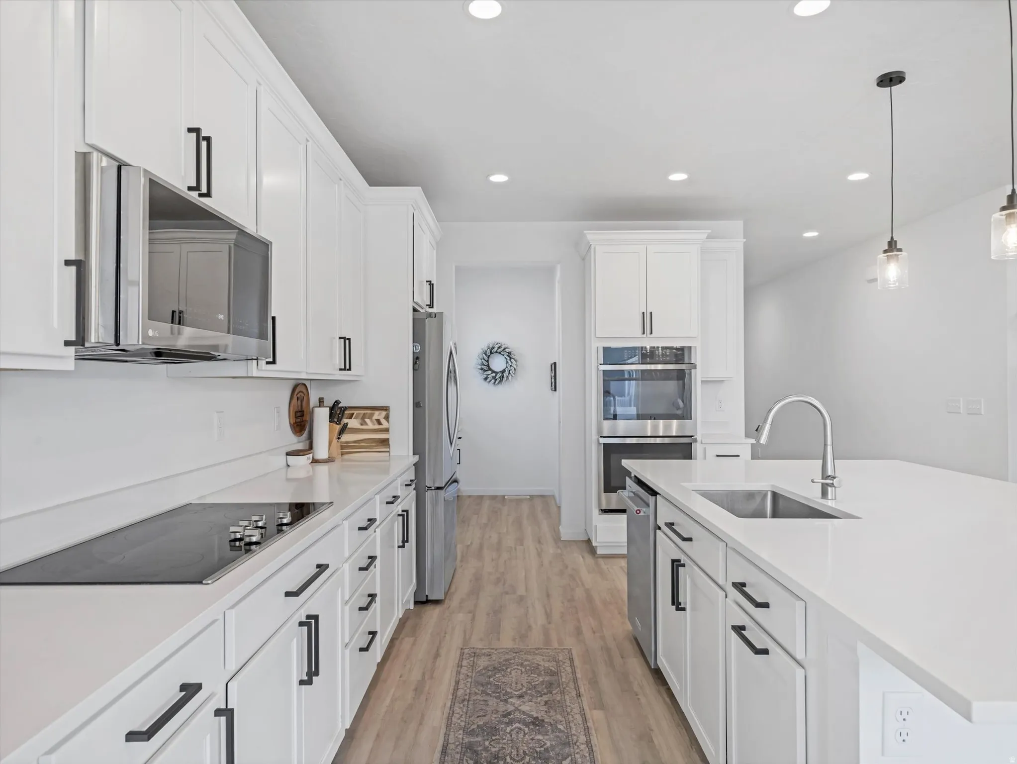 Contemporary kitchen featuring white cabinetry with matte black hardware, light-toned wood-finish flooring, recessed lighting, stainless steel appliances, and a central island with an undermount sink