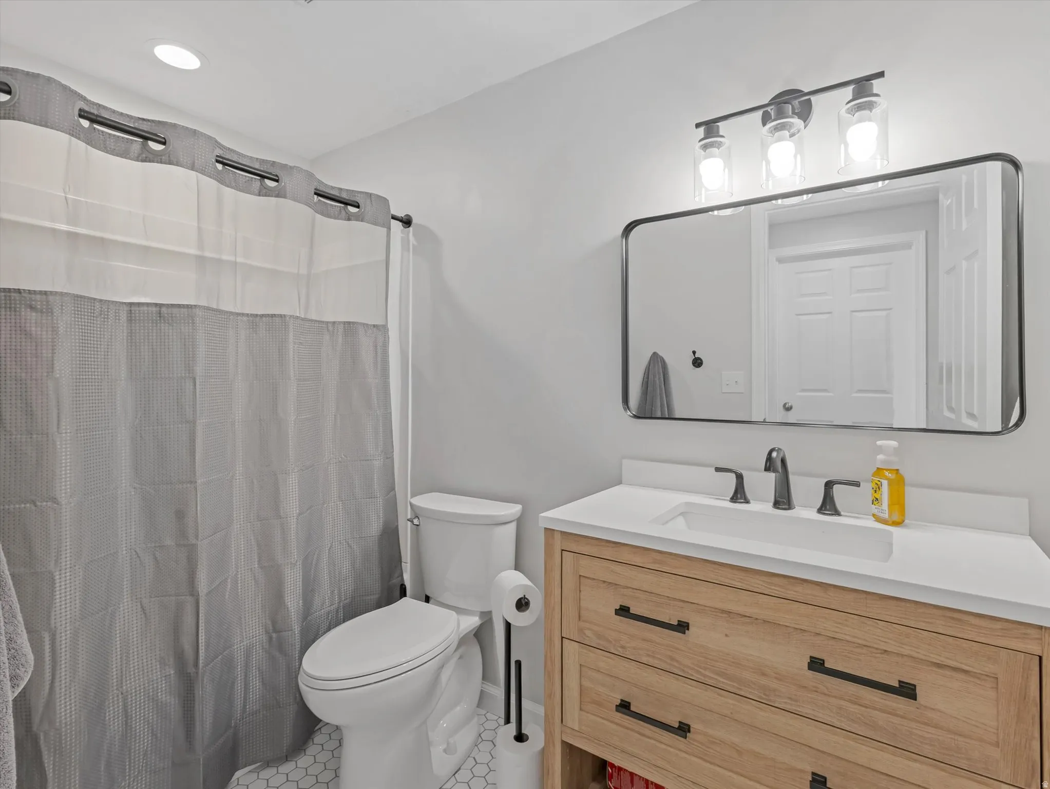 Modern bathroom featuring a wood-finish vanity with a rectangular undermount sink, a sleek black-framed mirror, and contemporary matte black fixtures