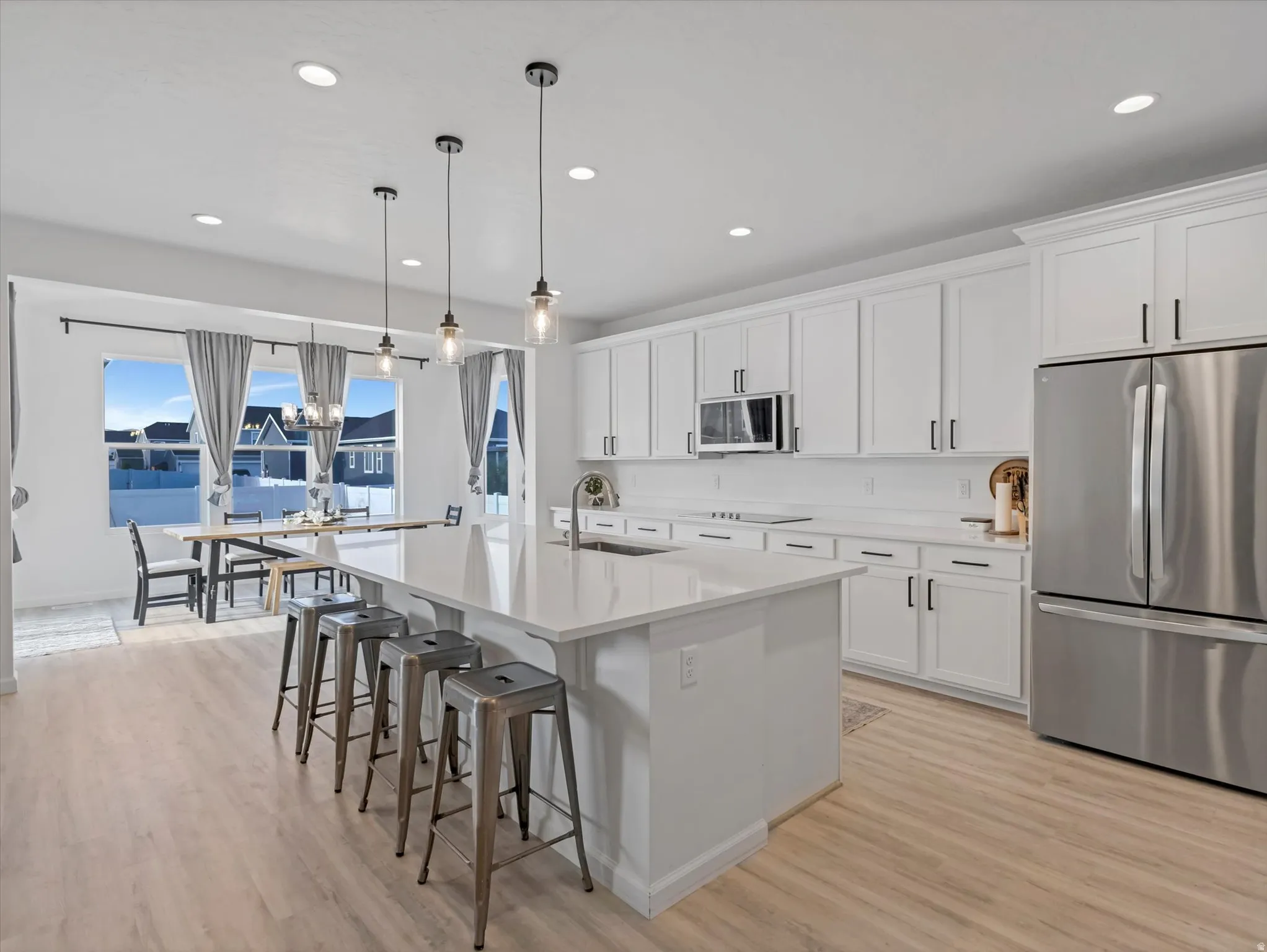 Open-concept kitchen featuring an expansive island with pendant lighting, white cabinetry, integrated stainless steel appliances, and wood-finish flooring