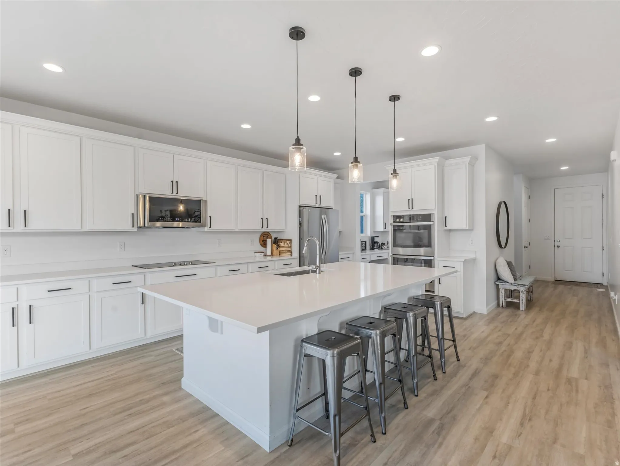 Open-concept kitchen featuring white cabinetry, stainless steel appliances, a large central island with seating, pendant lighting, and wood-finish flooring