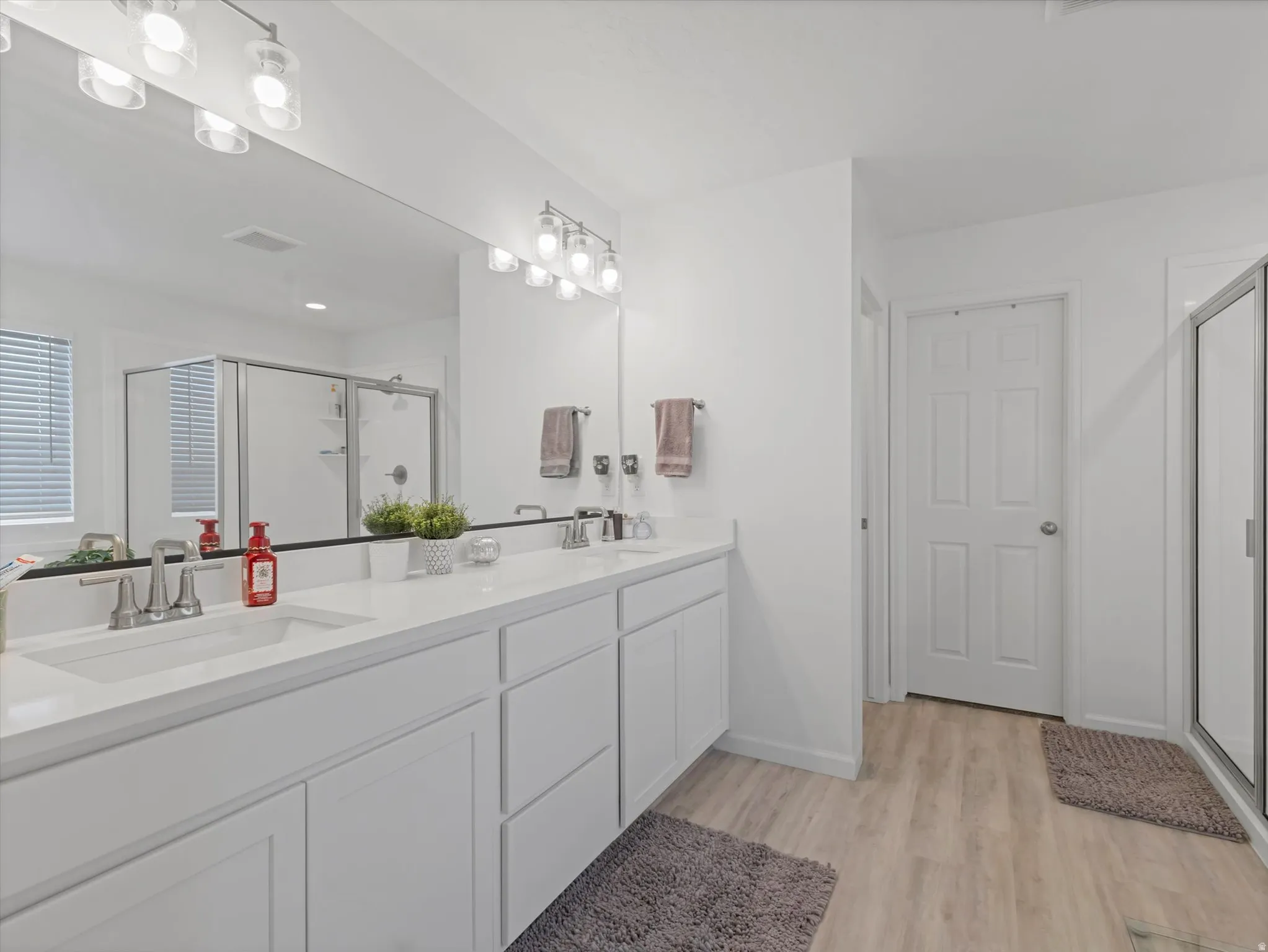 Bathroom featuring a dual vanity with white cabinetry and integrated sinks, a large wall-mounted mirror, and wood-finish flooring