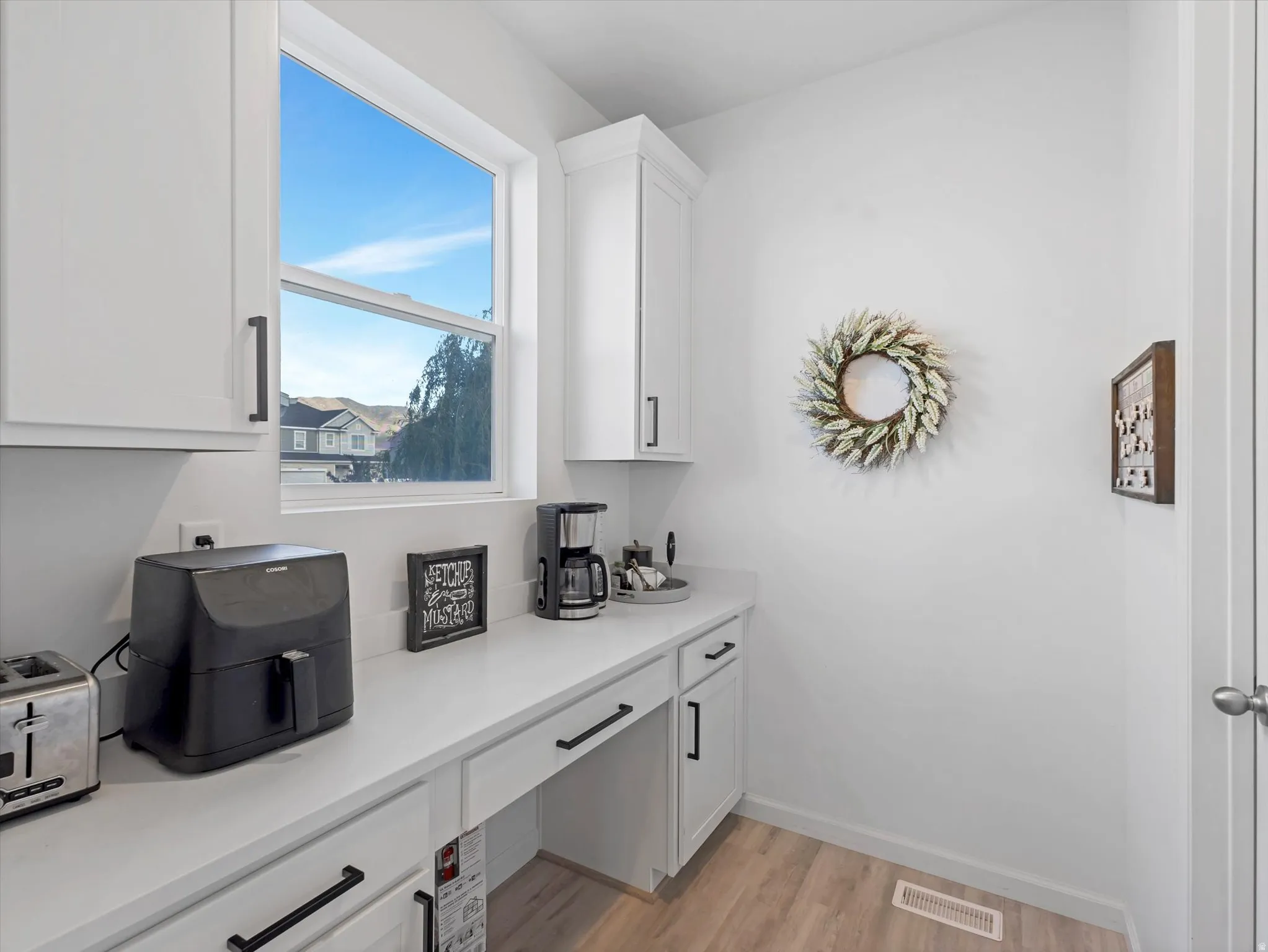 White cabinetry with matte black hardware, light-toned wood-finish flooring, and a window with exterior views