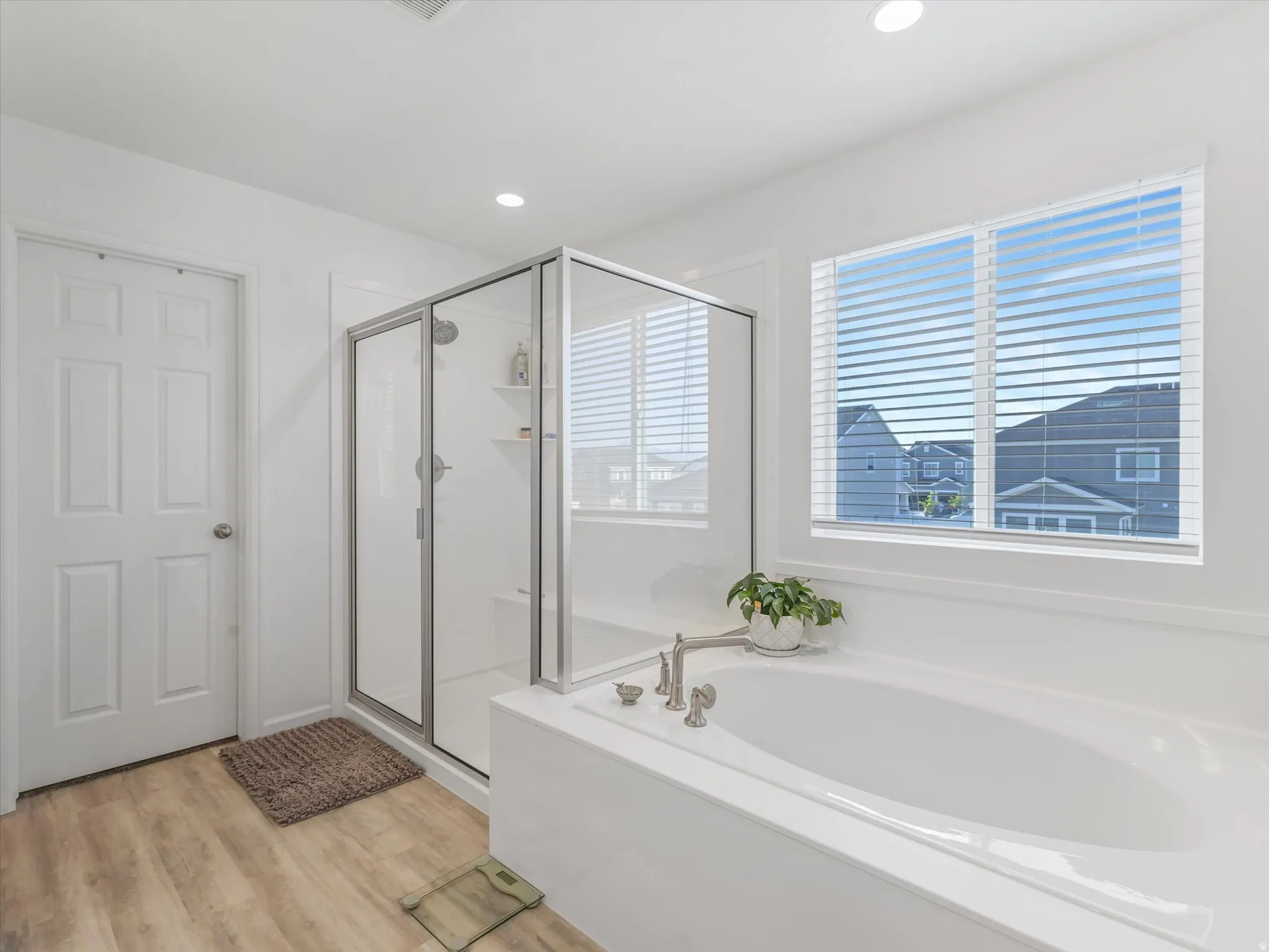 Soaking tub with brushed nickel fixtures, alongside a glass-enclosed shower featuring built-in shelving