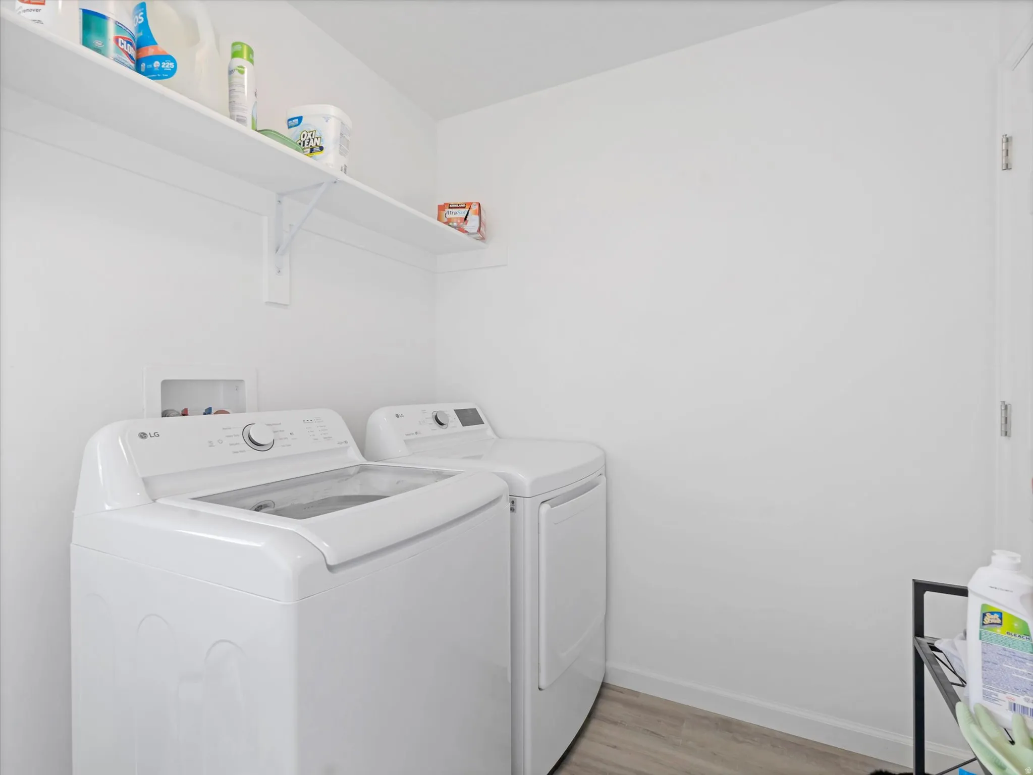 Dedicated laundry area featuring a wall-mounted storage shelf and wood-finish flooring