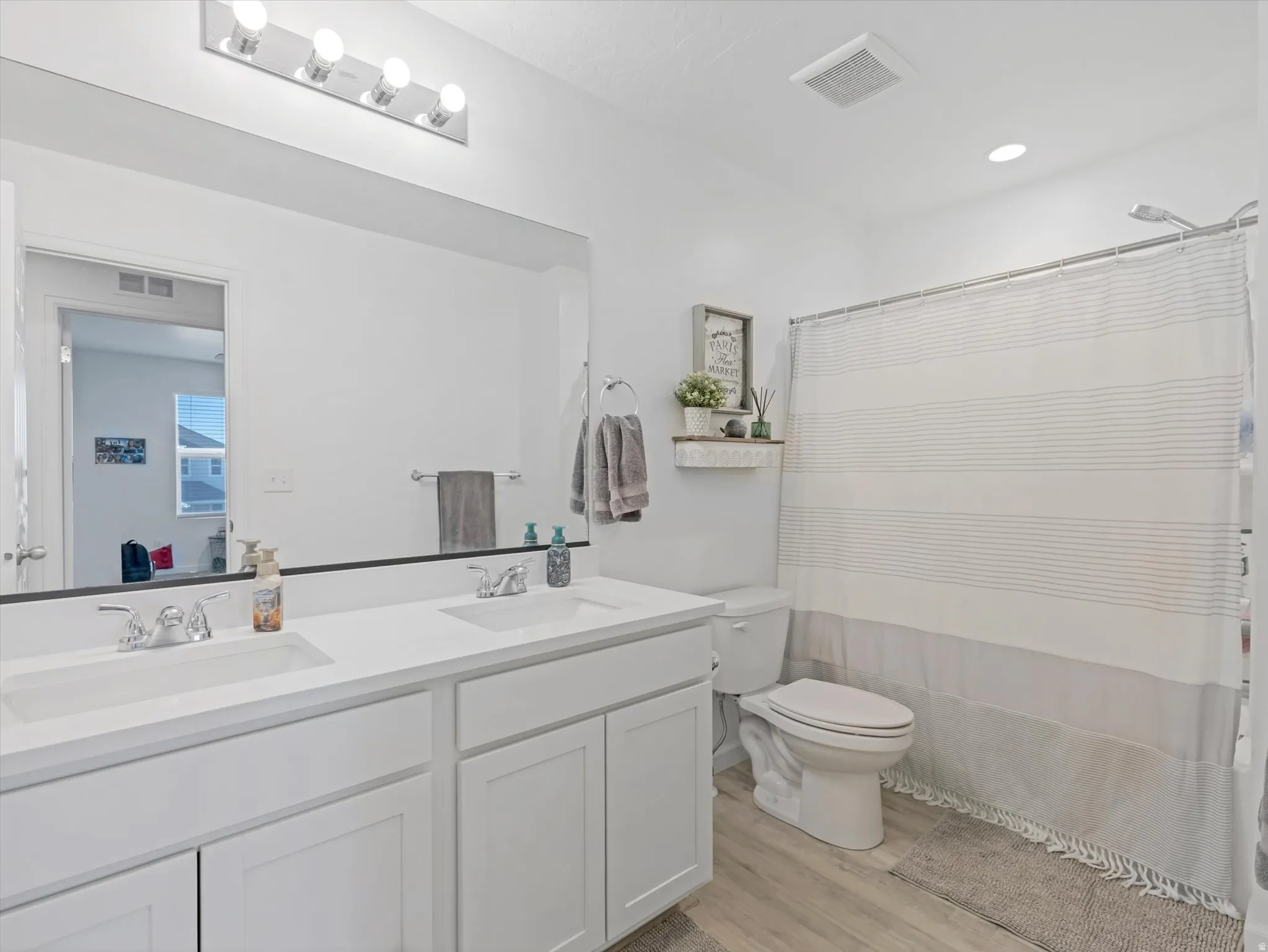 Bathroom with dual white vanities, integrated sinks, chrome faucets, and an expansive wall mirror