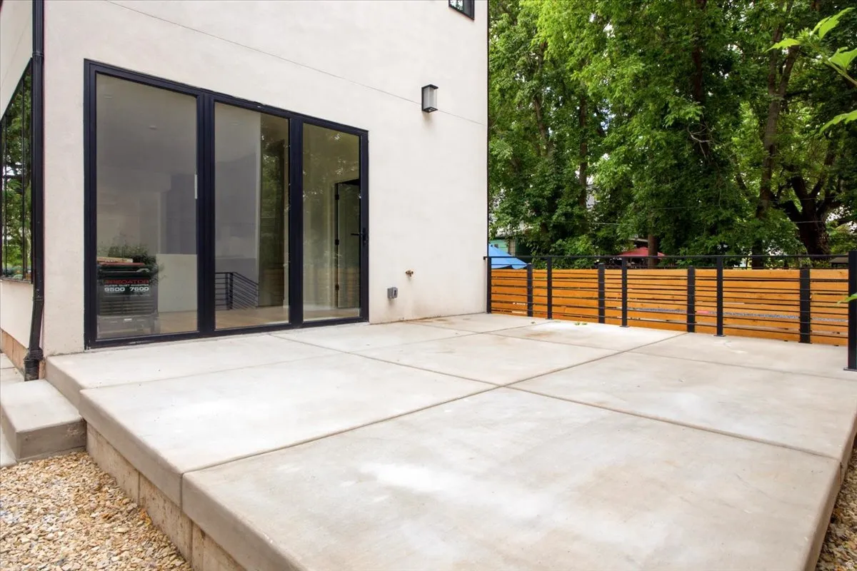 Expansive concrete patio featuring a modern horizontal slatted wood fence with dark metal posts, and large multi-panel glass doors