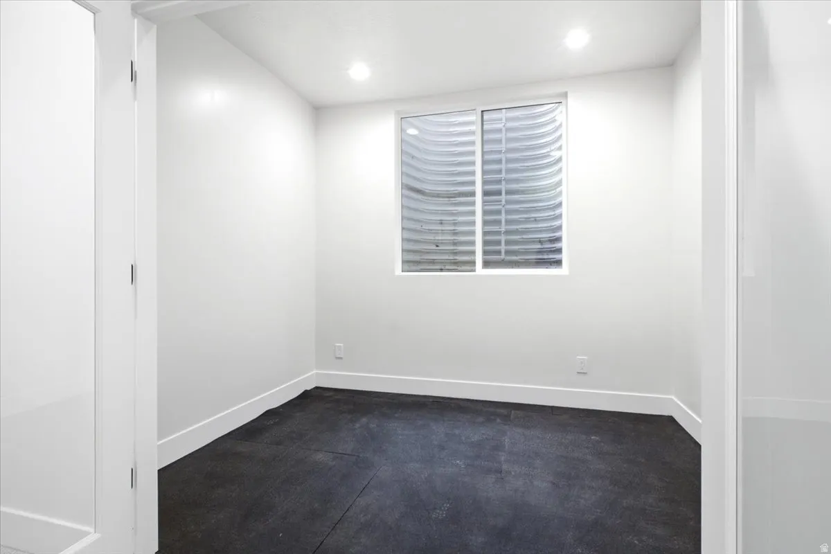 Room with clean white walls and dark flooring, featuring a window with a window well