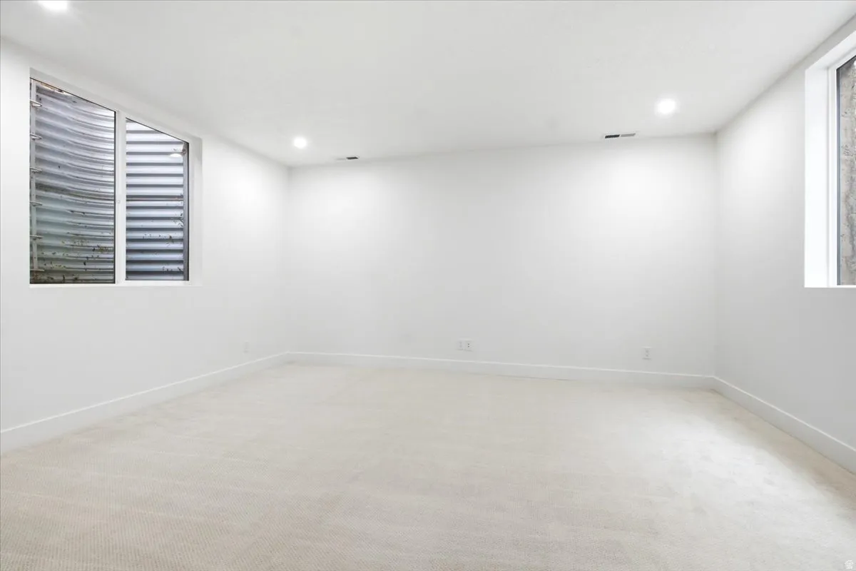 Spacious room featuring light-toned carpeting, crisp white walls, recessed ceiling lighting, and two egress windows