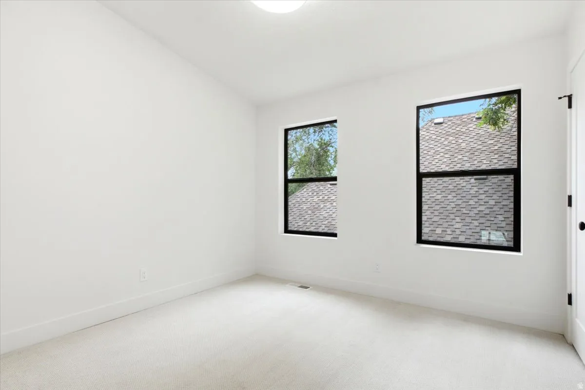 Bright room featuring two large windows with black frames, white walls, white trim, light-colored carpeting, and a flush-mount ceiling light