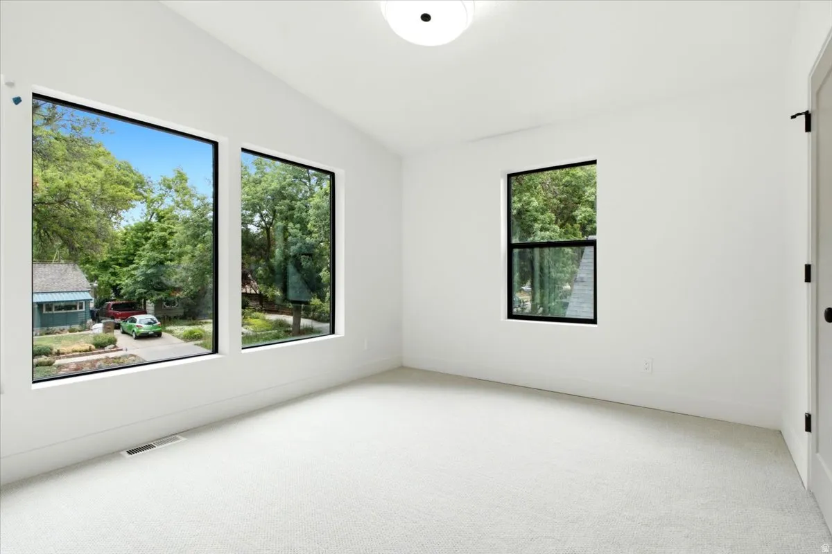 Bright interior space featuring three black-framed windows, white walls, and light-colored carpet