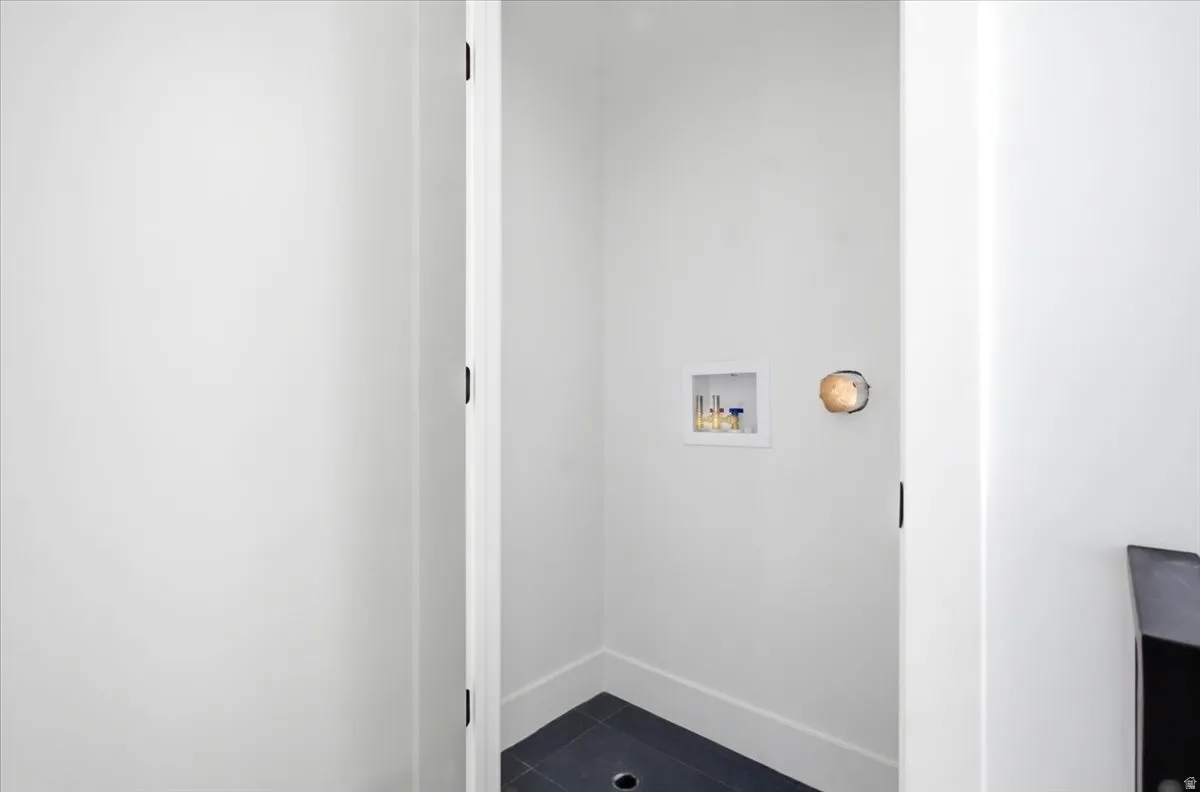 Dedicated laundry area featuring a wall-mounted utility box, dark tile flooring, and white baseboards