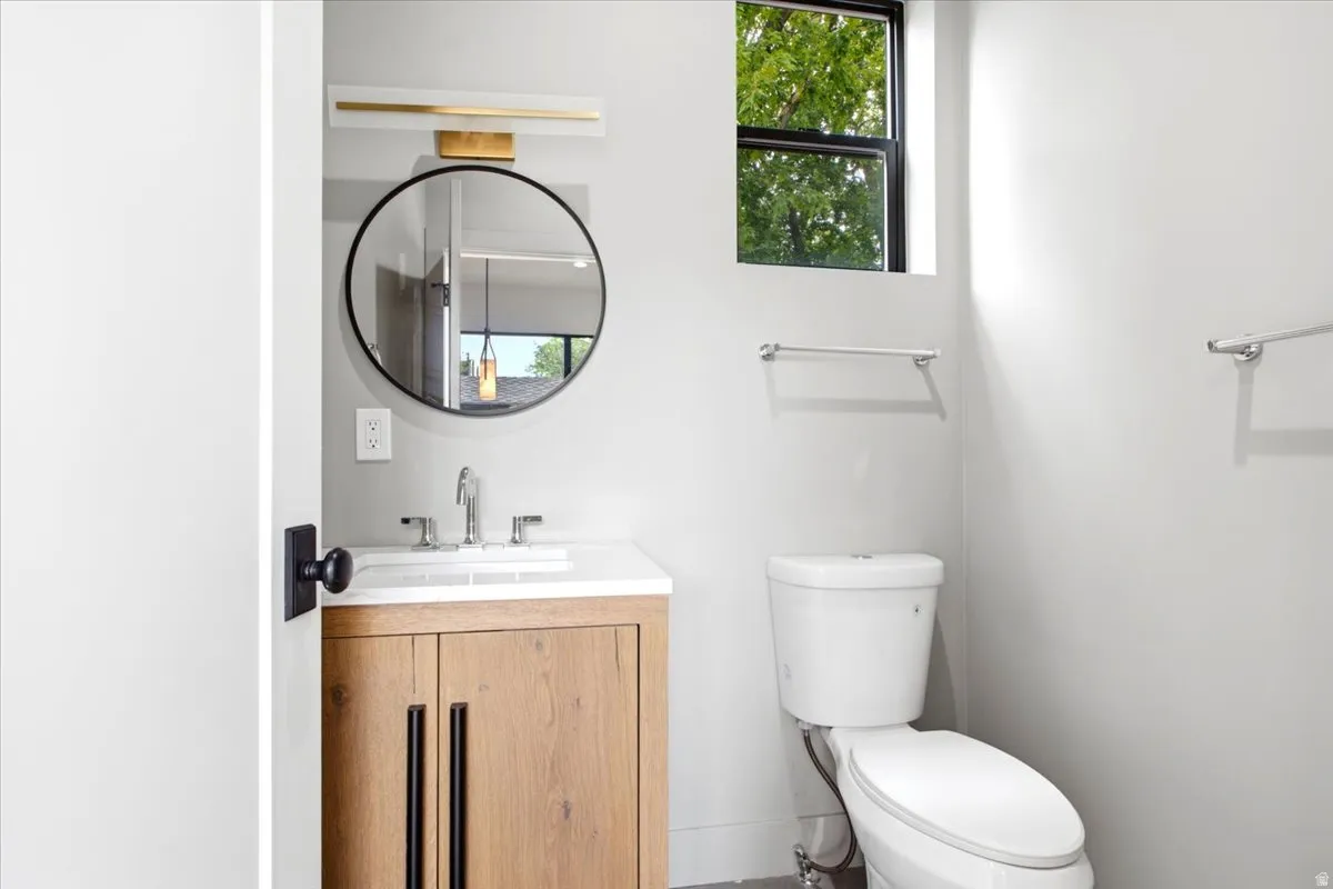 Powder room featuring a wood-finish vanity with a white countertop and undermount sink, a circular mirror, and modern wall-mounted lighting
