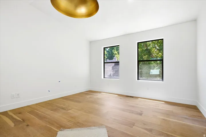 Spacious room featuring light wood-finish flooring, white walls, and a large gold-finish ceiling light fixture