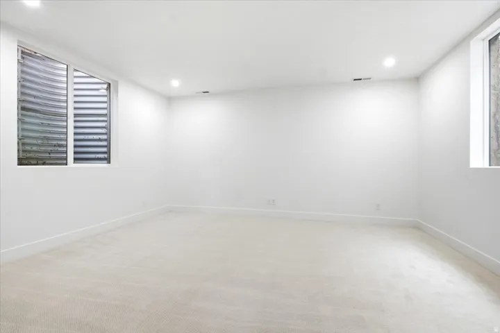Spacious room featuring light-toned carpeting, crisp white walls, recessed ceiling lighting, and two egress windows